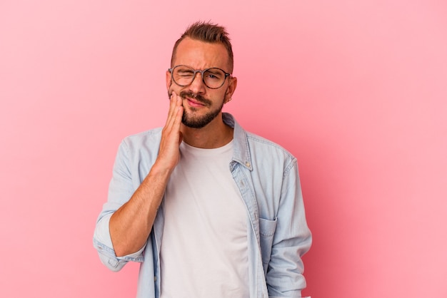 Hombre caucásico joven con tatuajes aislados sobre fondo rosa que tiene un fuerte dolor de dientes, dolor de muelas.