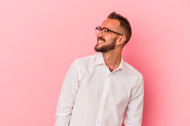 Hombre caucásico joven con tatuajes aislados sobre fondo rosa relajado y feliz riendo, cuello estirado mostrando los dientes.