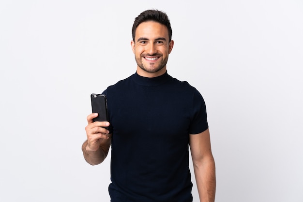 Hombre caucásico joven con teléfono móvil aislado en blanco sonriendo mucho