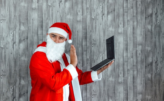 Hombre caucásico joven vestido como Santa Claus saludando en una videollamada en la computadora.