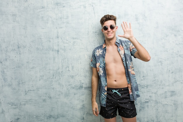 Hombre caucásico joven vistiendo un traje de baño sonriendo alegre mostrando el número cinco con los dedos.