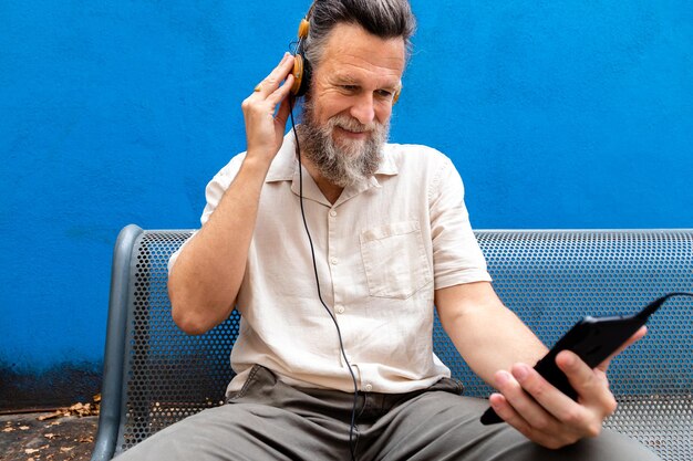 Hombre caucásico maduro escuchando música con auriculares usando el teléfono en el parque público. Concepto de estilo de vida. Actividad de ocio.