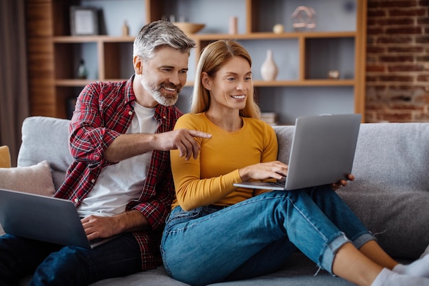 Un hombre caucásico maduro feliz mira a su esposa con una laptop chateando, ve un anuncio de video y ofrece en la sala de estar