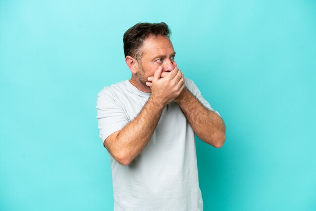 Hombre caucásico de mediana edad aislado de fondo azul cubriendo la boca y mirando hacia un lado