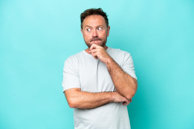 Hombre caucásico de mediana edad aislado de fondo azul con dudas y pensando