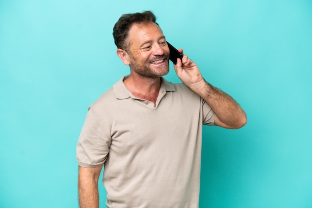 Hombre caucásico de mediana edad aislado de fondo azul manteniendo una conversación con el teléfono móvil