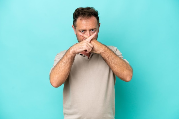 Hombre caucásico de mediana edad aislado de fondo azul que muestra un gesto de silencio