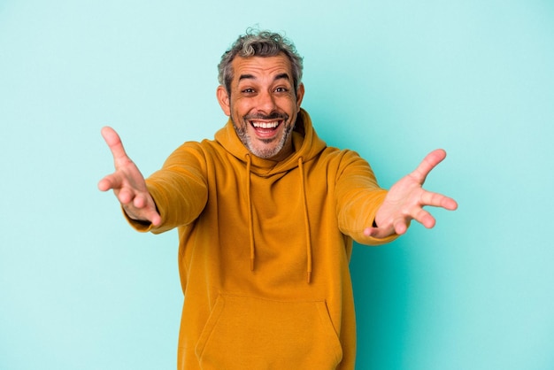 El hombre caucásico de mediana edad aislado de fondo azul se siente seguro dando un abrazo a la cámara.