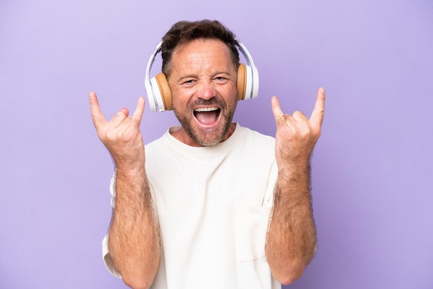 Hombre caucásico de mediana edad aislado de fondo morado escuchando música haciendo gestos de rock