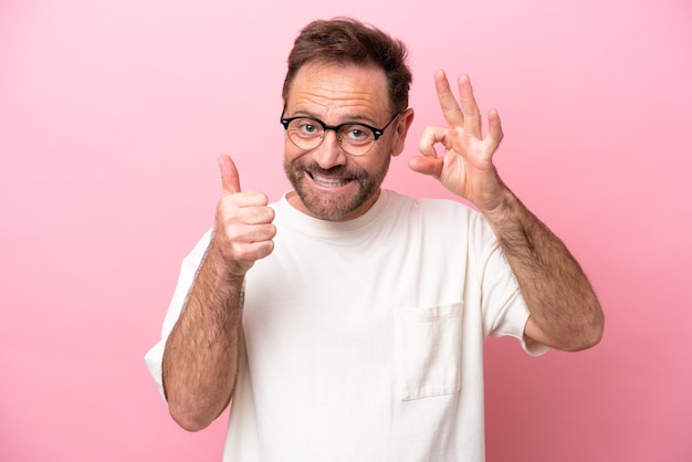 Hombre caucásico de mediana edad aislado de fondo rosa con gafas y haciendo el signo de OK