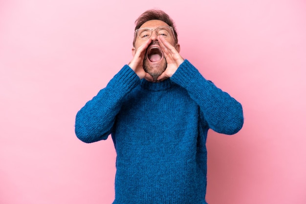 Hombre caucásico de mediana edad aislado de fondo rosa gritando y anunciando algo