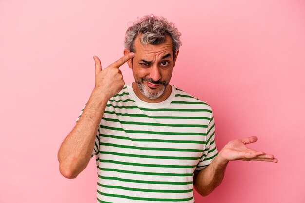 Hombre caucásico de mediana edad aislado de fondo rosa que muestra un gesto de decepción con el dedo índice.