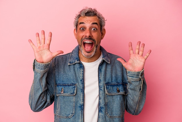 Hombre caucásico de mediana edad aislado de fondo rosa que recibe una agradable sorpresa, emocionado y levantando la mano.