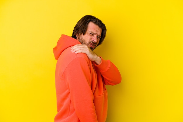 Hombre caucásico de mediana edad aislado en la pared amarilla con dolor en el hombro.