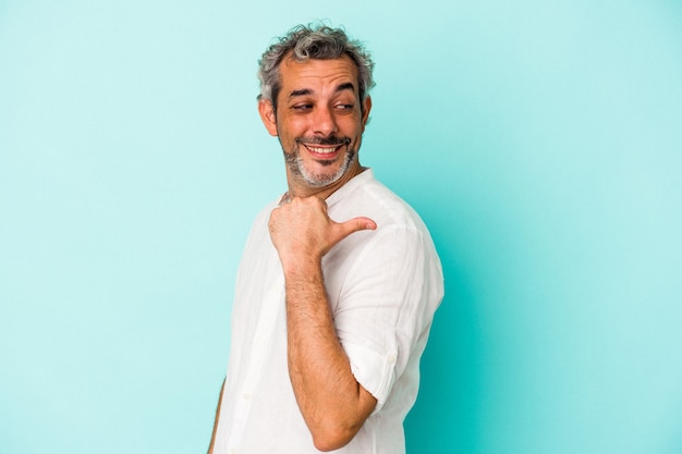 Hombre caucásico de mediana edad aislado en puntos de fondo azul con el dedo pulgar de distancia, riendo y despreocupado.