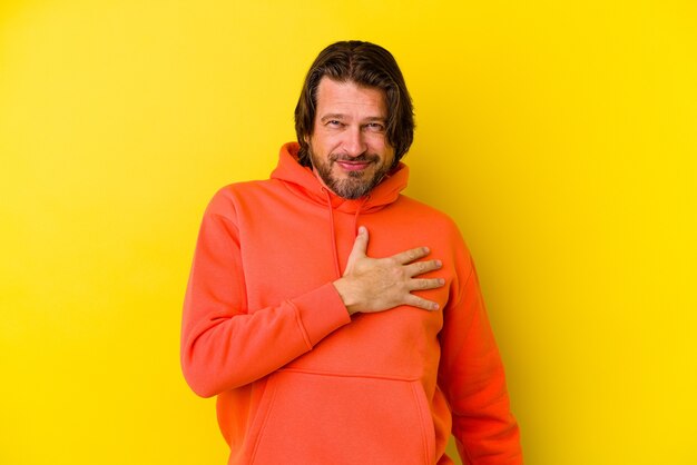 Hombre caucásico de mediana edad aislado sobre fondo amarillo tomando un juramento, poniendo la mano en el pecho.