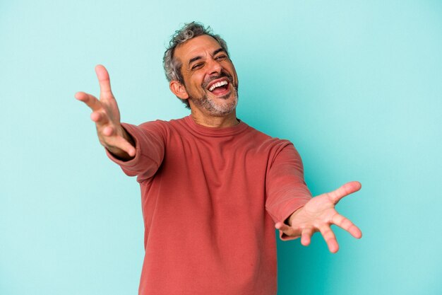 Hombre caucásico de mediana edad aislado sobre fondo azul se siente confiado dando un abrazo a la cámara.