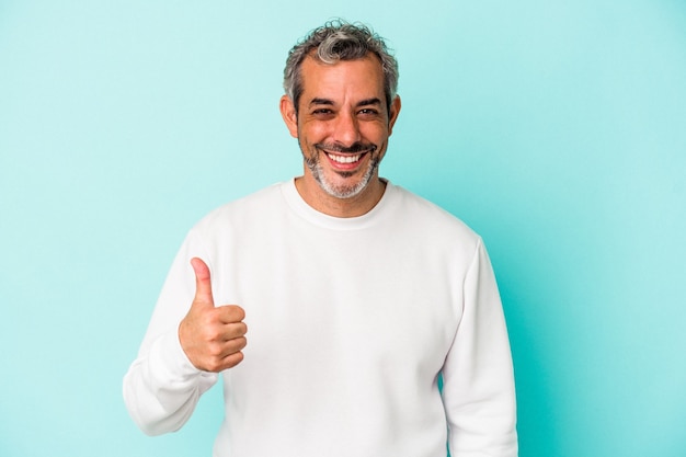 Hombre caucásico de mediana edad aislado sobre fondo azul sonriendo y levantando el pulgar hacia arriba