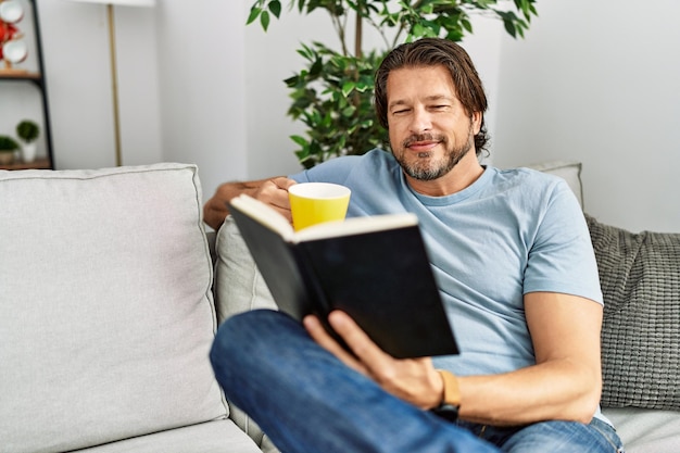 Hombre caucásico de mediana edad bebiendo café leyendo un libro en casa