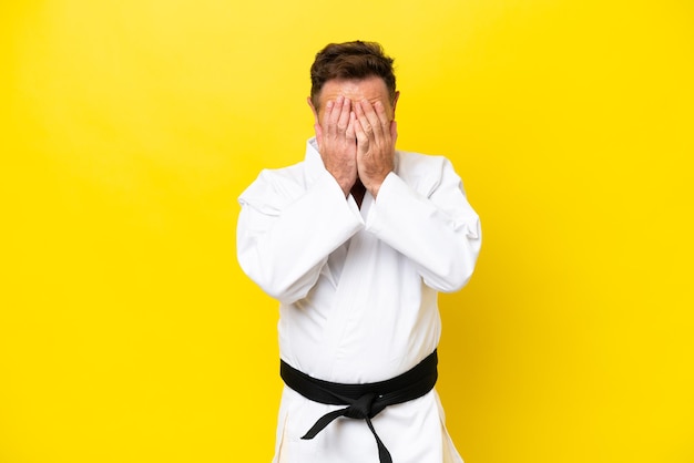 Hombre caucásico de mediana edad haciendo karate aislado de fondo amarillo con expresión cansada y enferma