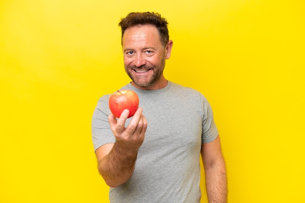 Hombre caucásico de mediana edad con una manzana aislada de fondo amarillo con expresión feliz