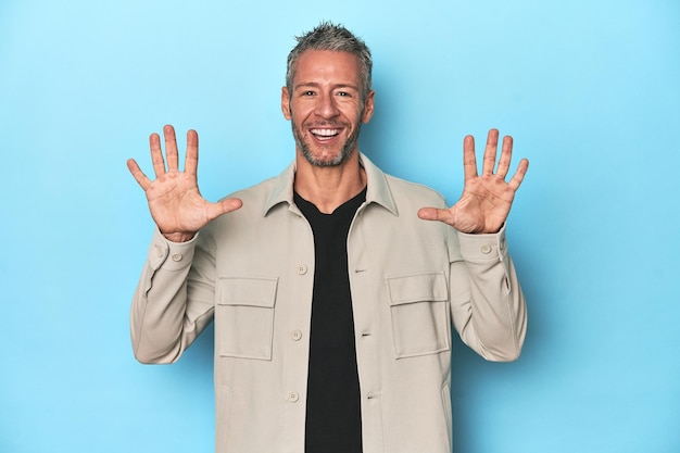 Hombre caucásico de mediana edad sobre fondo azul mostrando el número diez con las manos