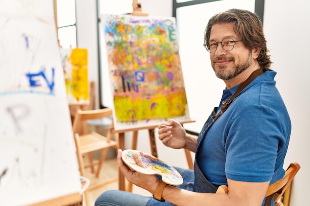 Hombre caucásico de mediana edad sonriendo confiado dibujando en el estudio de arte