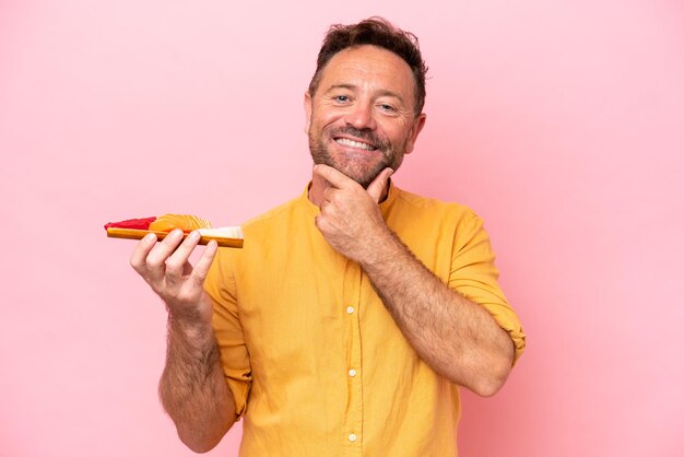 Hombre caucásico de mediana edad sosteniendo sashimi aislado sobre fondo rosa feliz y sonriente