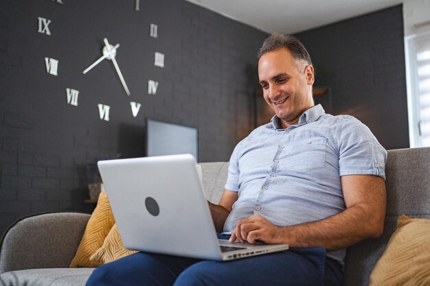 Hombre caucásico de mediana edad usando una computadora portátil en el sofá