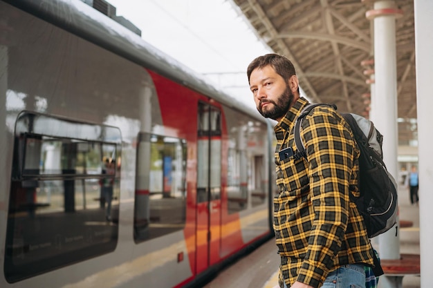 Hombre caucásico con mochila de pie en la plataforma que va a tomar el tren