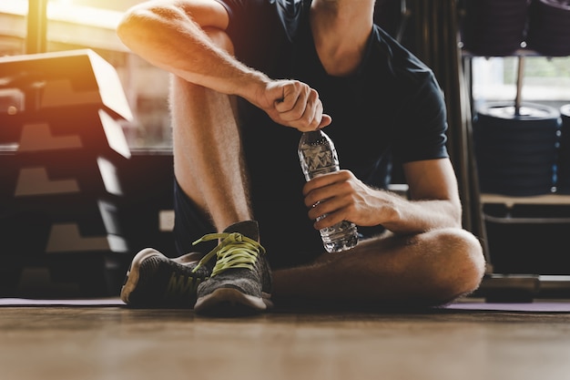 hombre caucásico musculoso tomando descanso relajarse bebiendo agua mientras descansa después de hacer ejercicio en el gimnasio