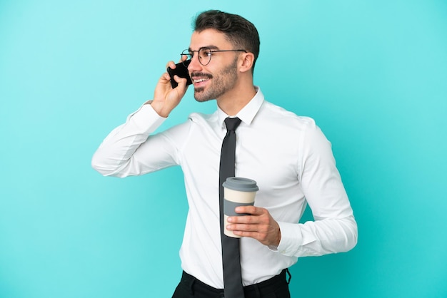 Hombre caucásico de negocios aislado sobre fondo azul con café para llevar y un móvil