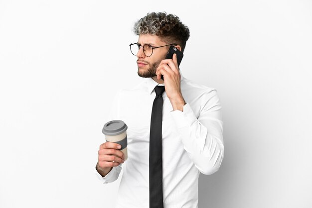 Hombre caucásico de negocios aislado sobre fondo blanco con café para llevar y un móvil