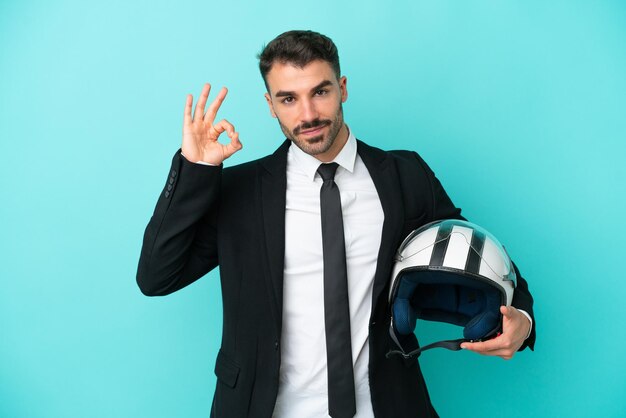 Hombre caucásico de negocios con casco de moto aislado sobre fondo azul que muestra el signo de ok con los dedos