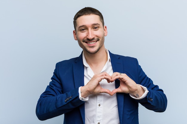 Hombre caucásico de negocios joven sonriendo y mostrando una forma de corazón con él las manos.