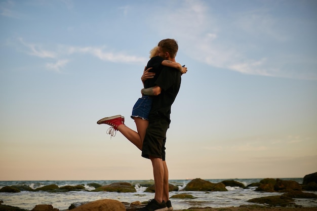 el hombre caucásico y la niña se abrazan a la orilla del mar en la playa al atardecer