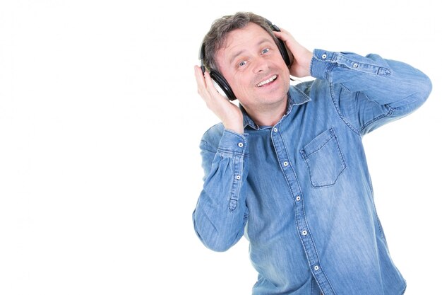 Hombre caucásico en la pared blanca escuchando música con auriculares y bailando