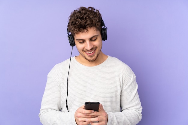 Hombre caucásico en pared púrpura escuchando música y mirando al móvil