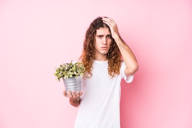 Hombre caucásico de pelo largo sosteniendo una planta en shock, ella ha recordado una reunión importante.