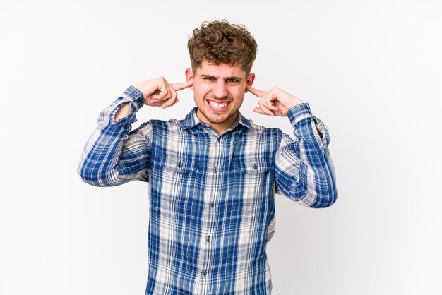 Foto hombre caucásico de pelo rizado rubio joven aislado cubriendo las orejas con las manos.