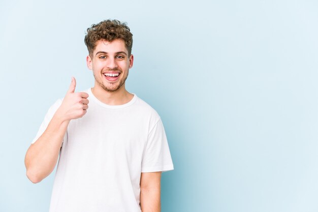 Hombre caucásico de pelo rizado rubio joven aislado sonriendo y levantando el pulgar hacia arriba