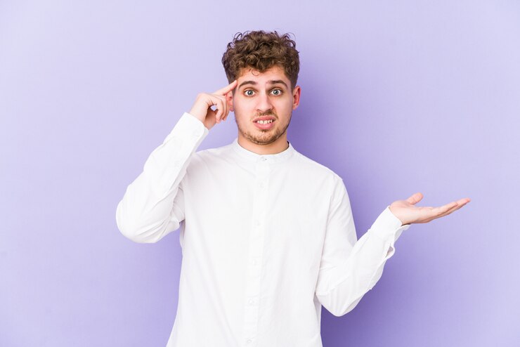 Foto hombre caucásico de pelo rizado rubio joven aislado sosteniendo y mostrando un producto en la mano.