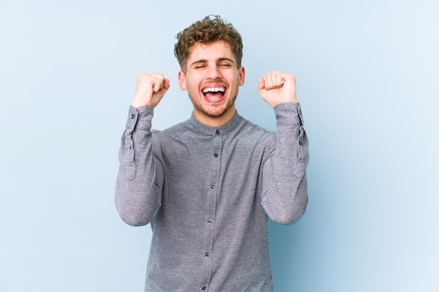 Hombre caucásico de pelo rizado rubio joven celebrando una victoria, pasión y entusiasmo, feliz expresión.