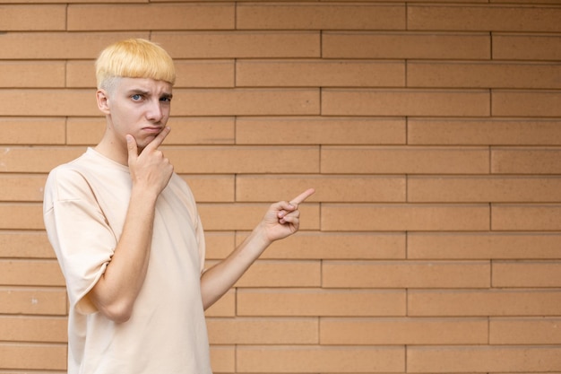 Un hombre caucásico pensante vestido con una camiseta beige señalando con el dedo el espacio de la copia