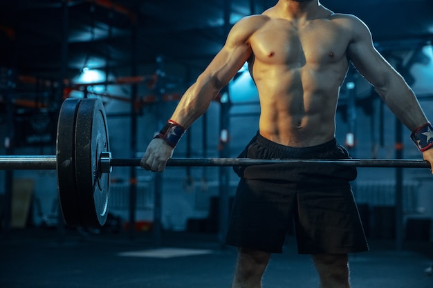 Hombre caucásico practicando levantamiento de pesas en el gimnasio. Entrenamiento de modelo deportivo masculino caucásico con barra, parece seguro y fuerte. Culturismo, estilo de vida saludable, movimiento, actividad, concepto de acción.