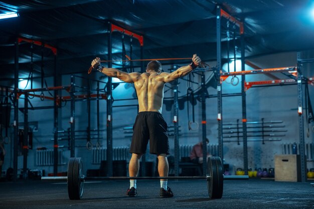 Hombre caucásico practicando levantamiento de pesas en el gimnasio. Entrenamiento de modelo deportivo masculino caucásico con barra, parece seguro y fuerte. Culturismo, estilo de vida saludable, movimiento, actividad, concepto de acción.