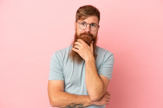 Hombre caucásico rojizo joven aislado en el pensamiento de fondo rosa