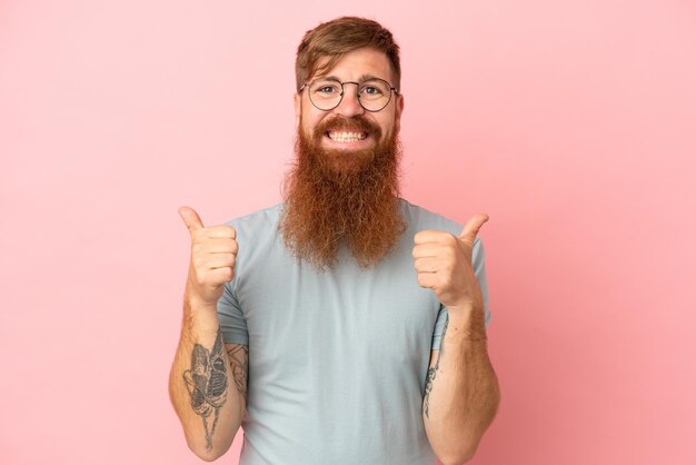 Hombre caucásico rojizo joven aislado sobre fondo rosa con pulgares arriba gesto y sonriendo