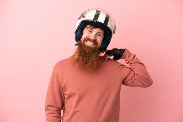 Hombre caucásico rojizo joven con un casco de motocicleta aislado sobre fondo rosa riendo