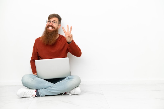 Hombre caucásico rojizo joven con portátil aislado sobre fondo blanco feliz y contando tres con los dedos